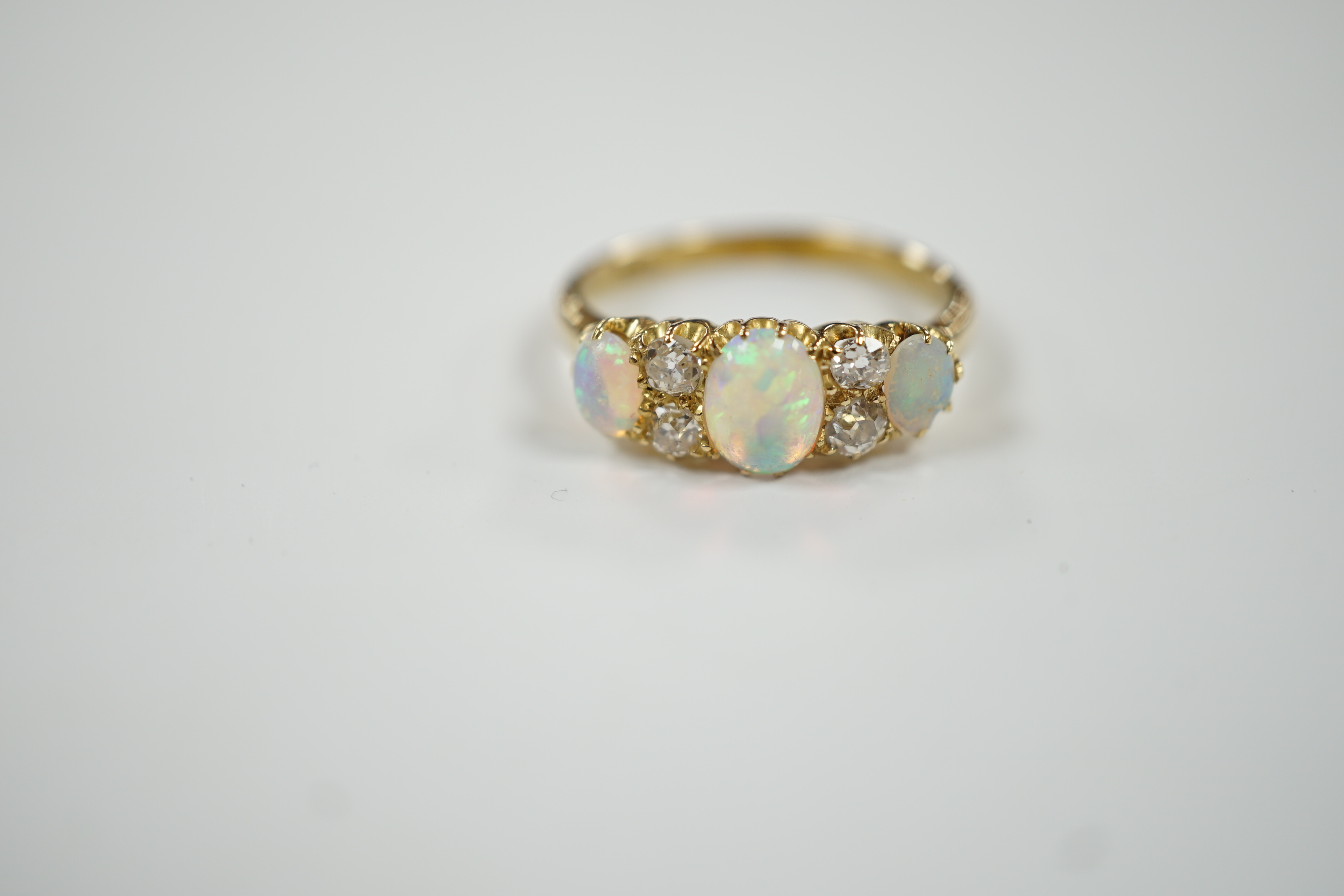 A yellow metal (tests as 18ct), three stone white opal and four stone diamond set half hoop ring, size N/O, gross weight 3.5 grams.